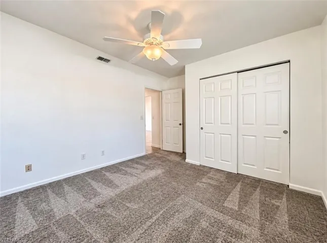 Neutral carpeting, white paneled closet doors, ceiling fan with integrated light fixture, and interior doors