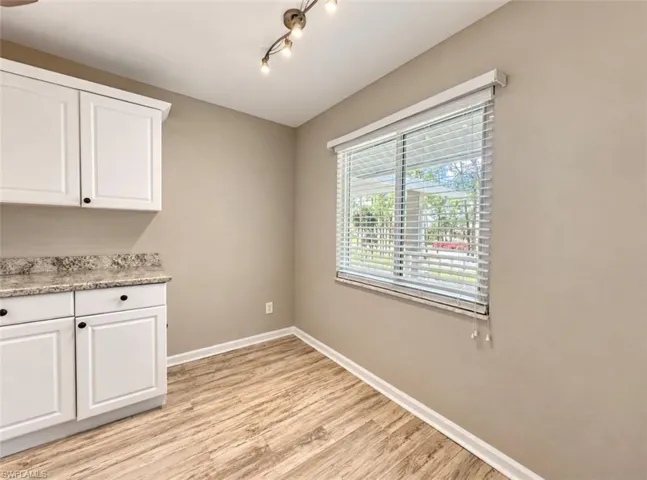 White cabinetry with stone-patterned countertops, wood-finish flooring, multi-bulb ceiling lighting, and a window with horizontal blinds