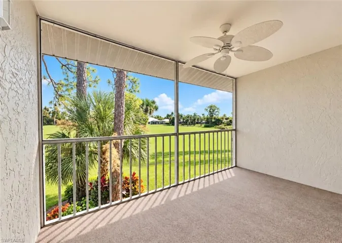 Screened-in balcony featuring a neutral textured wall finish, overhead paddle fan, and metal railings overlooking green space with mature landscaping