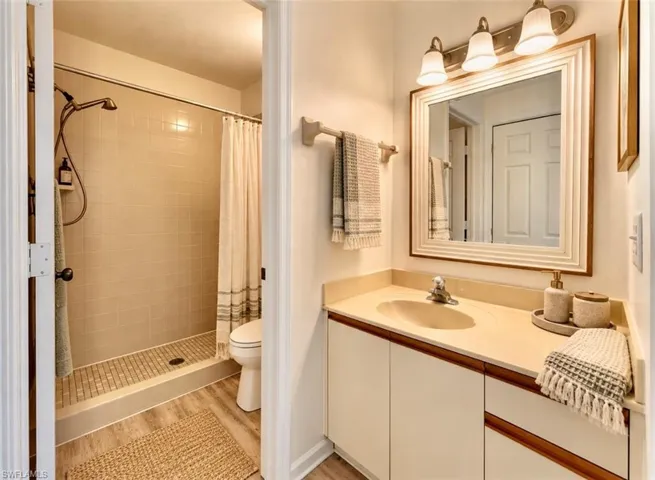 B**Virtually staged athroom featuring a vanity with integrated sink, framed wall mirror, triple-bulb vanity light, shower with tiled walls and flooring, and wood-finish flooring