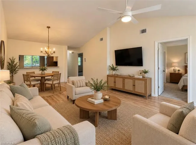 **Virtually staged Open-concept interior featuring vaulted ceilings, wood-finish flooring, a contemporary chandelier, and a ceiling fan with integrated lighting