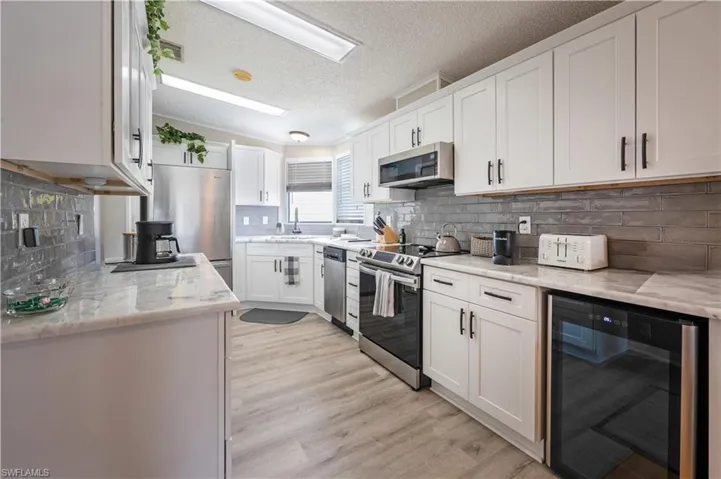 Kitchen featuring wine cooler, appliances with stainless steel finishes, a sink, white cabinetry, and light wood-type flooring