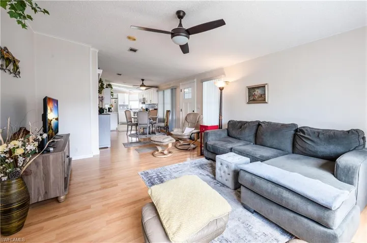 Living room with ceiling fan, light wood-style flooring, a textured ceiling, and baseboards