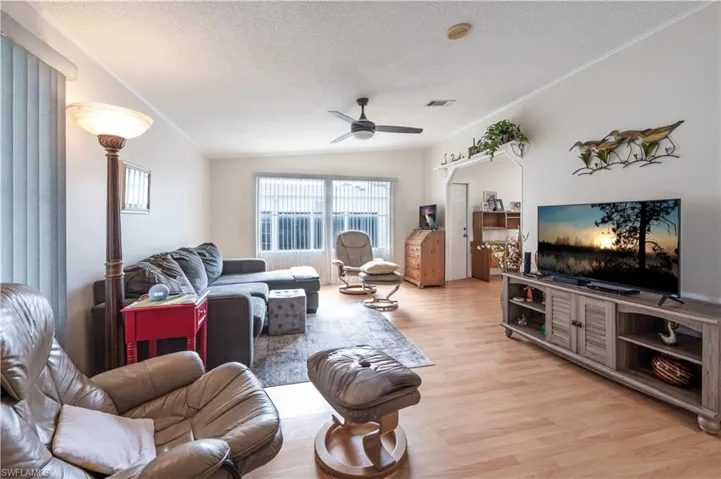 Living area featuring a textured ceiling, a ceiling fan, light wood finished floors, and vaulted ceiling