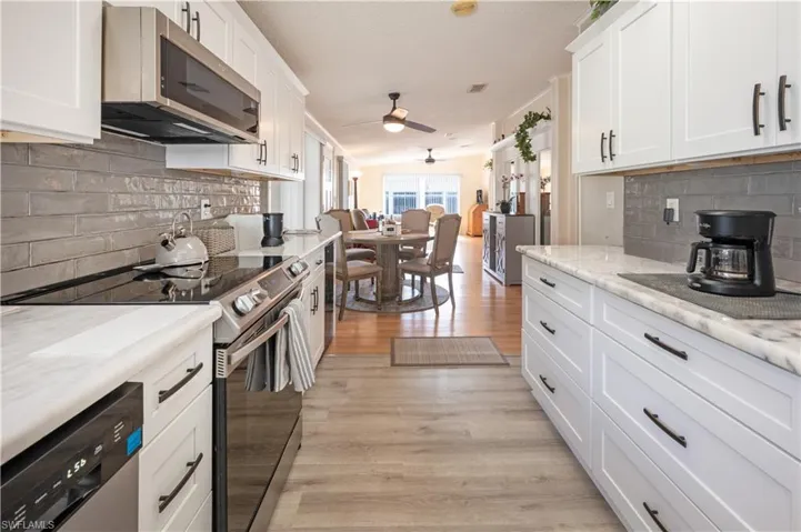 Kitchen with appliances with stainless steel finishes, ceiling fan, light wood-type flooring, white cabinetry, and tasteful backsplash