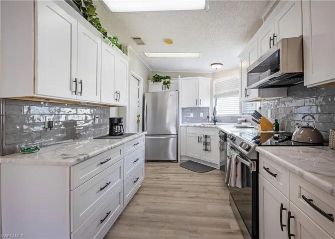 Kitchen with stainless steel appliances, tasteful backsplash, white cabinets, a sink, and light wood-style floors