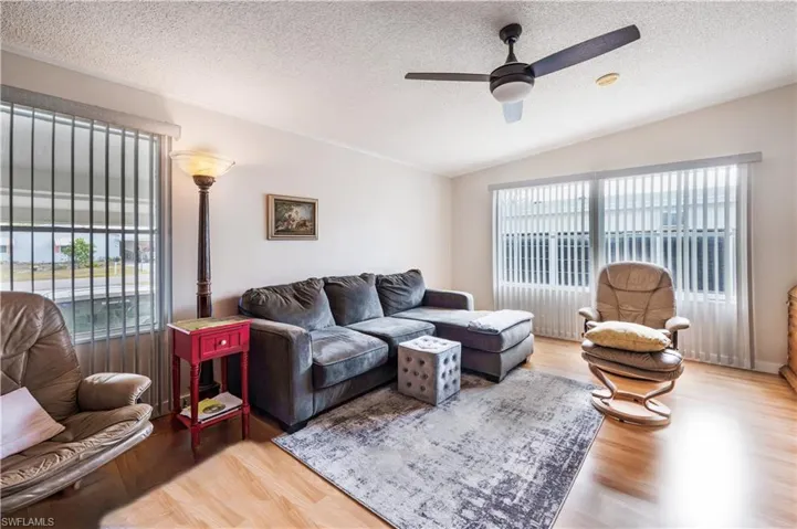 Living area with wood finished floors, vaulted ceiling, a ceiling fan, and a textured ceiling