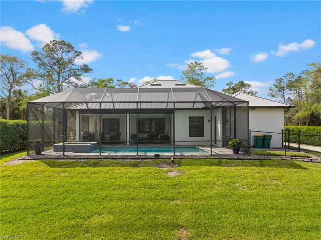 Back of house featuring a yard, stucco siding, fence, and a lanai
