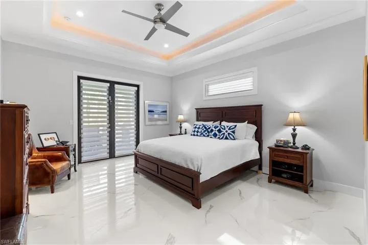Bedroom with marble finish floor, access to outside, a tray ceiling, and baseboards