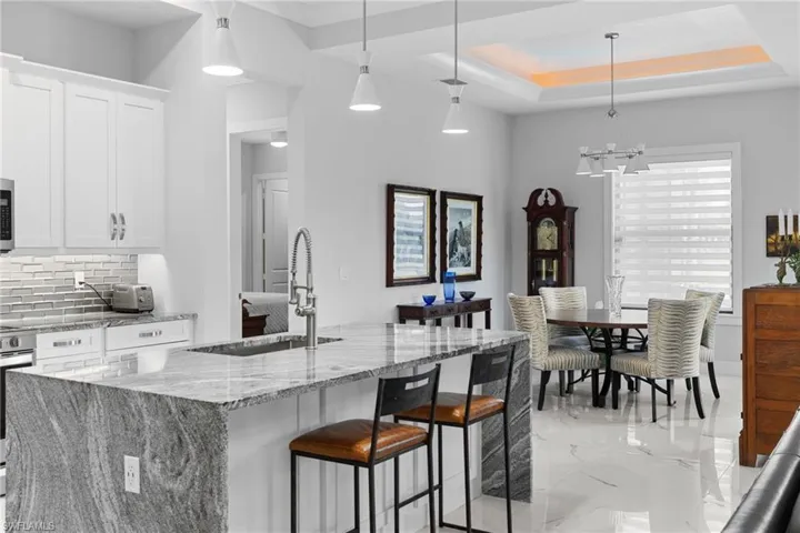 Kitchen featuring a sink, white cabinets, marble finish floor, backsplash, and a raised ceiling