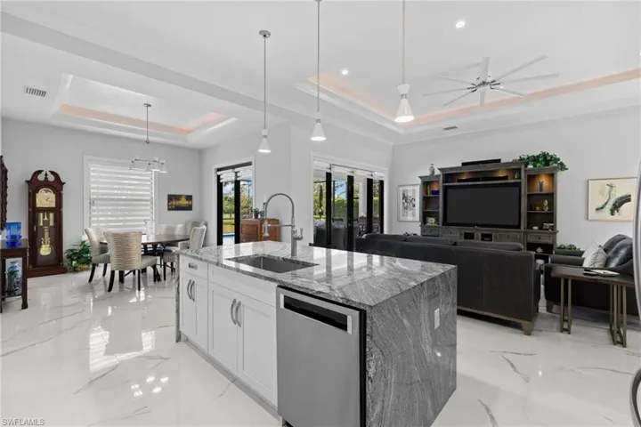 Kitchen with light stone counters, a sink, marble finish floor, stainless steel dishwasher, and a raised ceiling