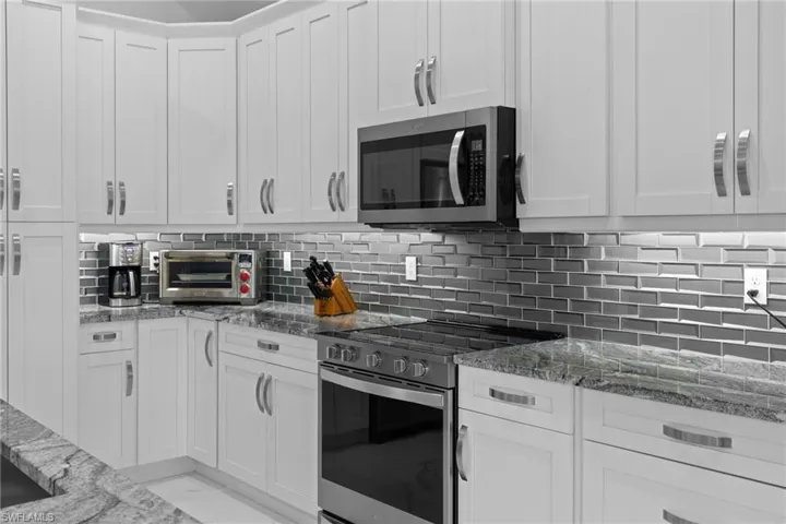 Kitchen with stone counters, white cabinetry, marble finish floor, appliances with stainless steel finishes, and decorative backsplash