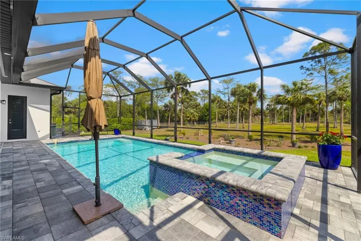 View of pool featuring glass enclosure, a pool with connected hot tub, and a patio