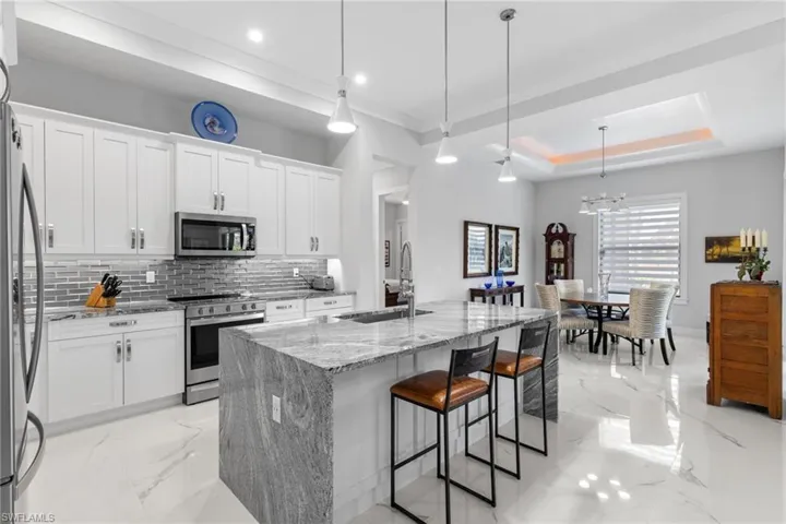 Kitchen with a tray ceiling, marble finish floor, stainless steel appliances, a sink, and light stone countertops