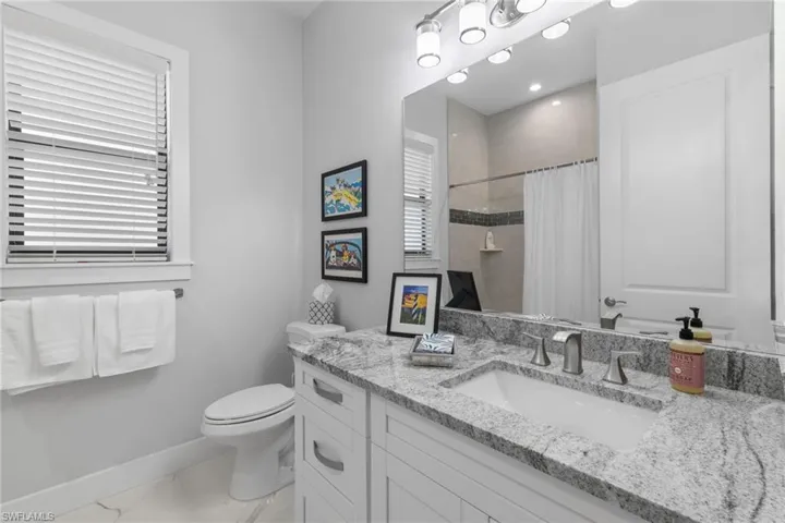 Bathroom with toilet, vanity, baseboards, marble finish floor, and a shower with curtain