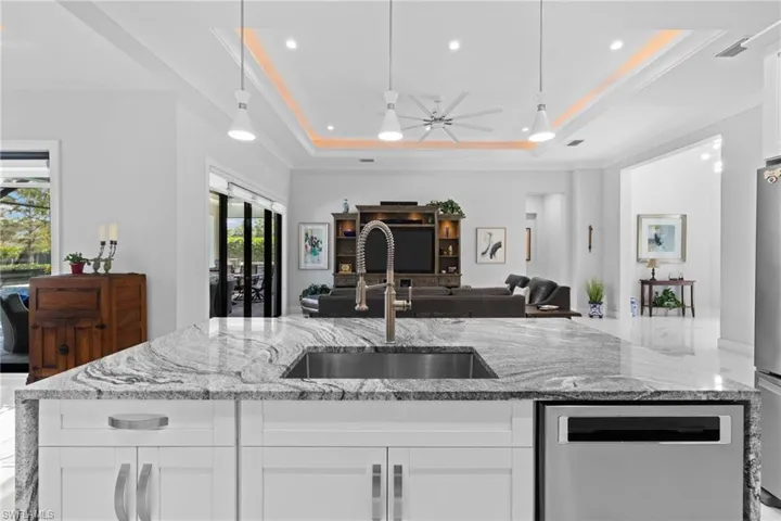 Kitchen with a sink, visible vents, open floor plan, a tray ceiling, and an island with sink