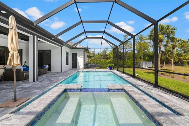 View of swimming pool featuring a patio, a pool with connected hot tub, a lawn, a lanai, and an outdoor living space