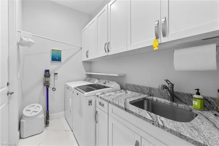 Laundry room featuring cabinet space, baseboards, marble finish floor, separate washer and dryer, and a sink