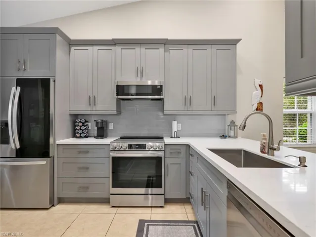 Kitchen with gray cabinetry, stainless steel appliances, light stone counters, light tile patterned floors, and lofted ceiling
