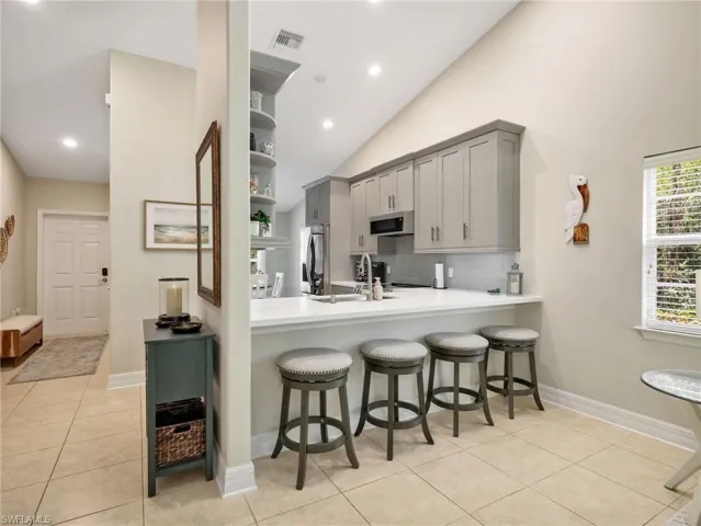 Kitchen featuring a breakfast bar, light tile patterned floors, gray cabinetry, backsplash, and vaulted ceiling