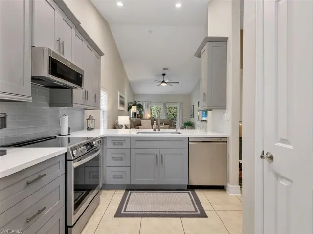 Kitchen with gray cabinets, stainless steel appliances, open floor plan, lofted ceiling, and light tile patterned floors