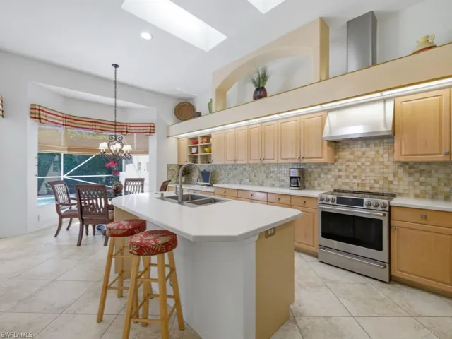 Kitchen with stainless steel electric range, ventilation hood, light tile patterned floors, and light countertops