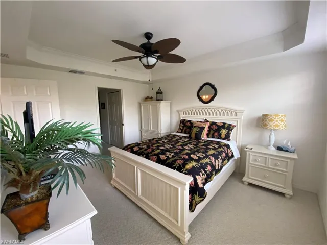 Bedroom with a tray ceiling, light carpet, ornamental molding, and ceiling fan