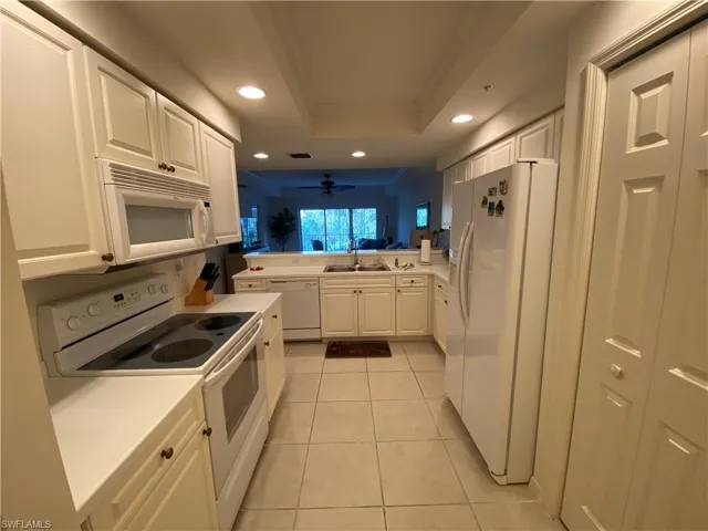 Kitchen with white appliances, white cabinets, a ceiling fan, a peninsula, and recessed lighting