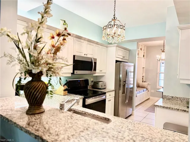 Kitchen featuring light stone countertops, stainless steel appliances, hanging light fixtures, a chandelier, and white cabinetry
