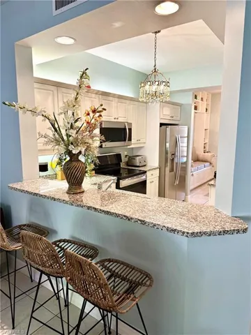 Kitchen featuring light stone countertops, a kitchen bar, stainless steel appliances, hanging light fixtures, and a peninsula