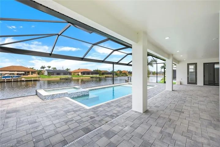 View of swimming pool featuring glass enclosure, a water view, a patio area, and an in ground hot tub