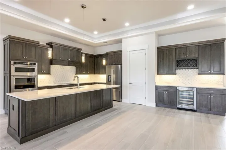 Kitchen featuring hanging light fixtures, appliances with stainless steel finishes, light hardwood / wood-style floors, sink, and wine cooler