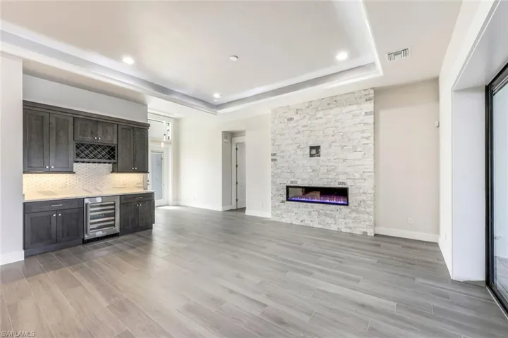 Unfurnished living room with light wood-type flooring, a fireplace, beverage cooler, and a tray ceiling