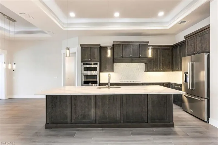 Kitchen with appliances with stainless steel finishes, sink, pendant lighting, and a center island with sink