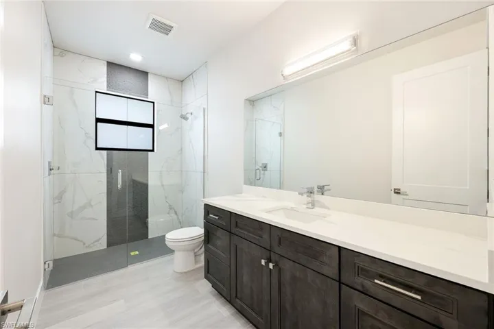Bathroom featuring a shower with door, vanity, and toilet