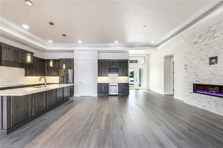 Kitchen with hardwood / wood-style floors, a raised ceiling, beverage cooler, pendant lighting, and dark brown cabinetry