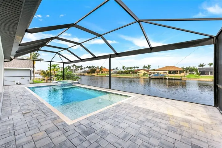 View of pool featuring glass enclosure, a patio, an in ground hot tub, and a water view