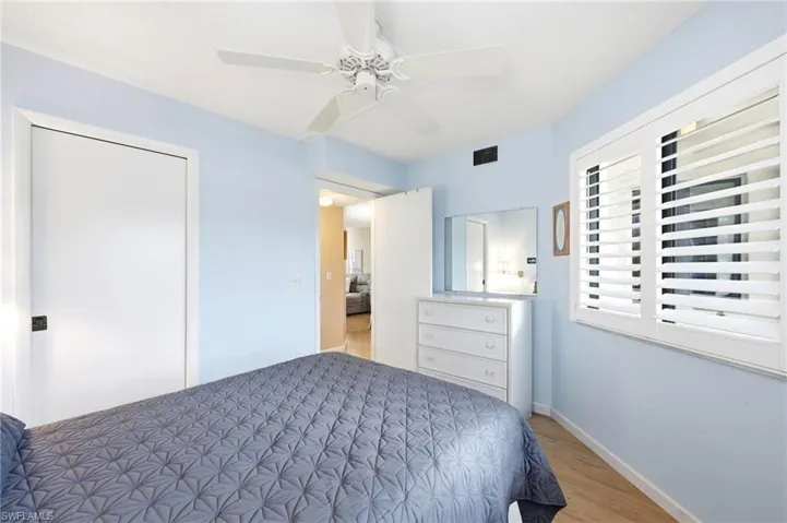Bedroom featuring wood-finish flooring, a ceiling fan, and window with plantation shutters