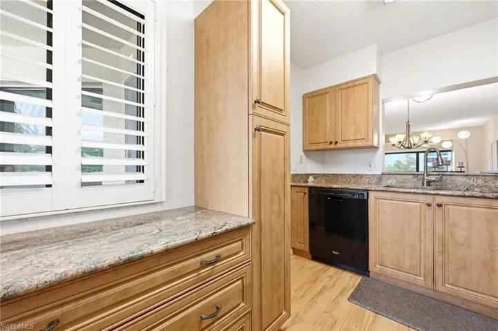 Kitchen featuring light wood-finish cabinetry, speckled countertops, stainless steel sink, and a black dishwasher