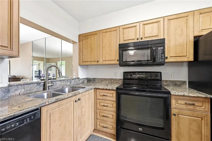 Kitchen featuring wood cabinetry, stone countertops, double basin stainless steel sink, black electric range, and black built-in microwave