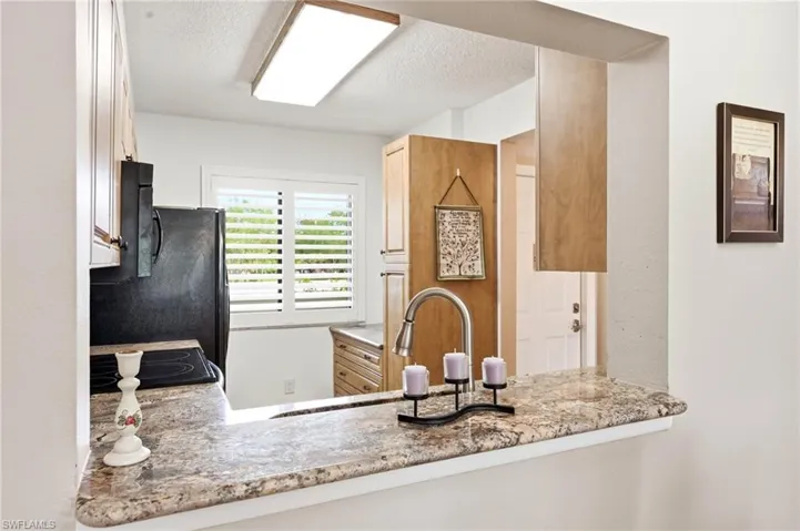 Kitchen featuring a pass-through window with granite-finish countertops, wood cabinetry, a stainless steel faucet, and a black refrigerator