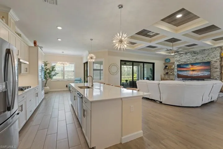 Kitchen with ornamental molding, white cabinetry, wood tiled floors, stainless steel appliances, and an island with sink