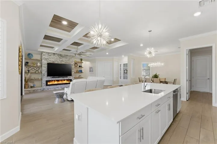 Kitchen featuring white cabinetry, a center island with sink, a chandelier, ornamental molding, and open floor plan