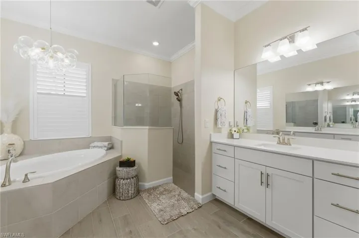 Bathroom with vanity, a walk in shower, a bath, suspended lighting, and ornamental molding