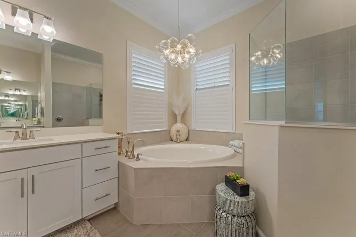 Bathroom featuring vanity, a garden tub, walk in shower, crown molding, and hanging lights