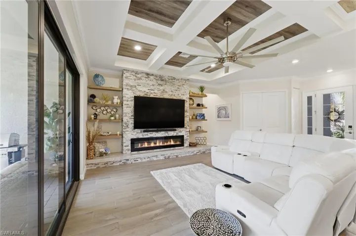 Living area featuring coffered ceiling, light wood-style floors, ornamental molding, ceiling fan, and a large fireplace