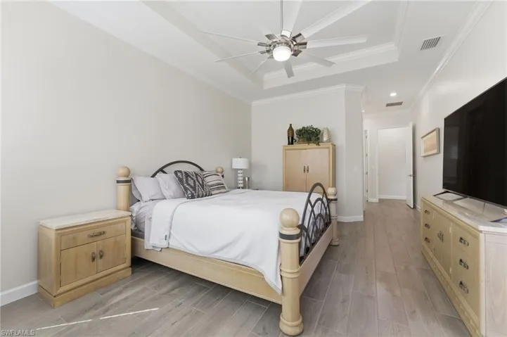 Bedroom with wood tiled floors, a ceiling fan, ornamental molding, and a raised ceiling
