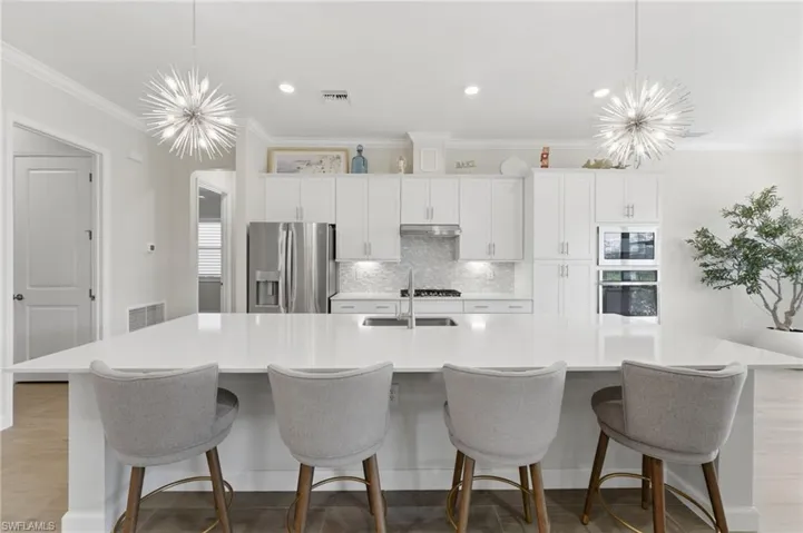 Kitchen with suspended lighting, white cabinetry, a spacious island, stainless steel appliances, and crown molding