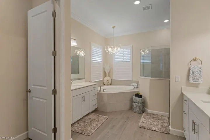 Full bathroom featuring crown molding, light wood finished floors, a bath, two vanities, and a walk in shower