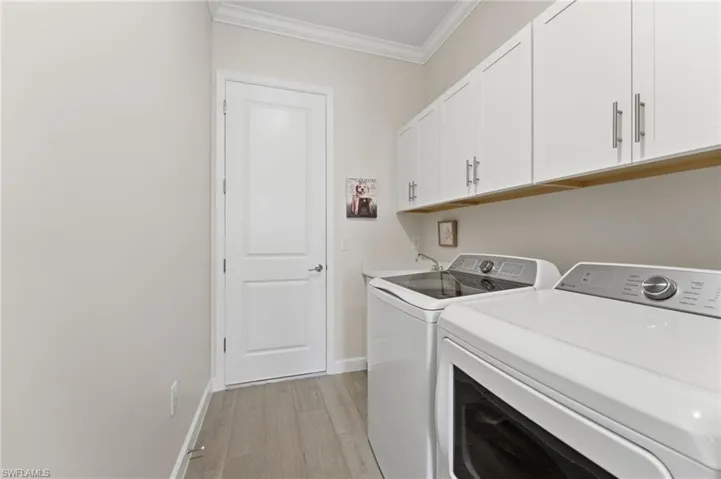 Laundry room with ornamental molding, independent washer and dryer, light wood-type flooring, and cabinet space